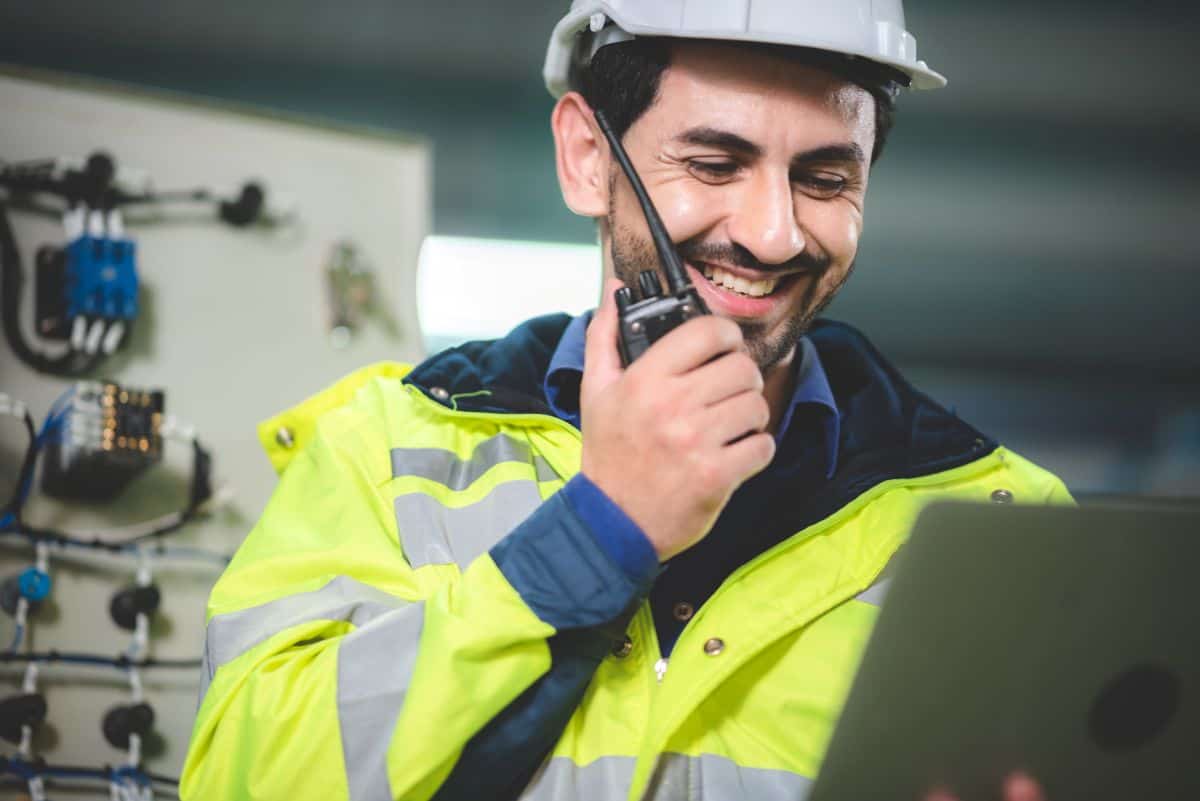 Un homme blanc en blouson de sécurité et casque de chantier parle dans un talkie-walkie