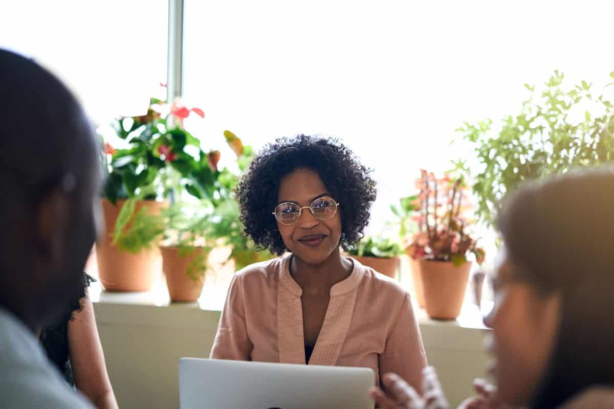 Une femme noire aux cheveux courts portant des lunettes assise à une table sourit