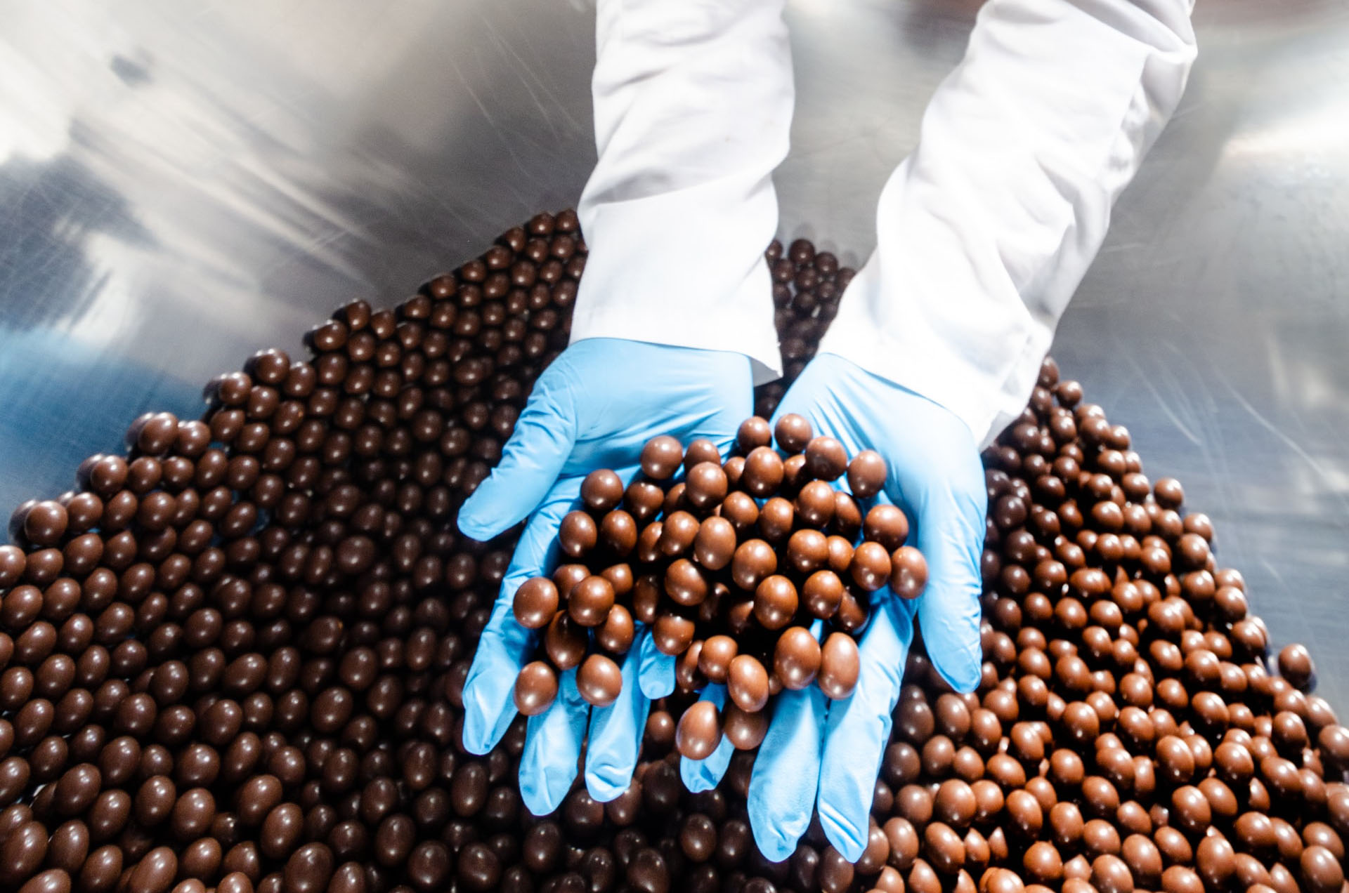 Une personne en blouse blanche prend dans ses mains gantées des billes de chocolat