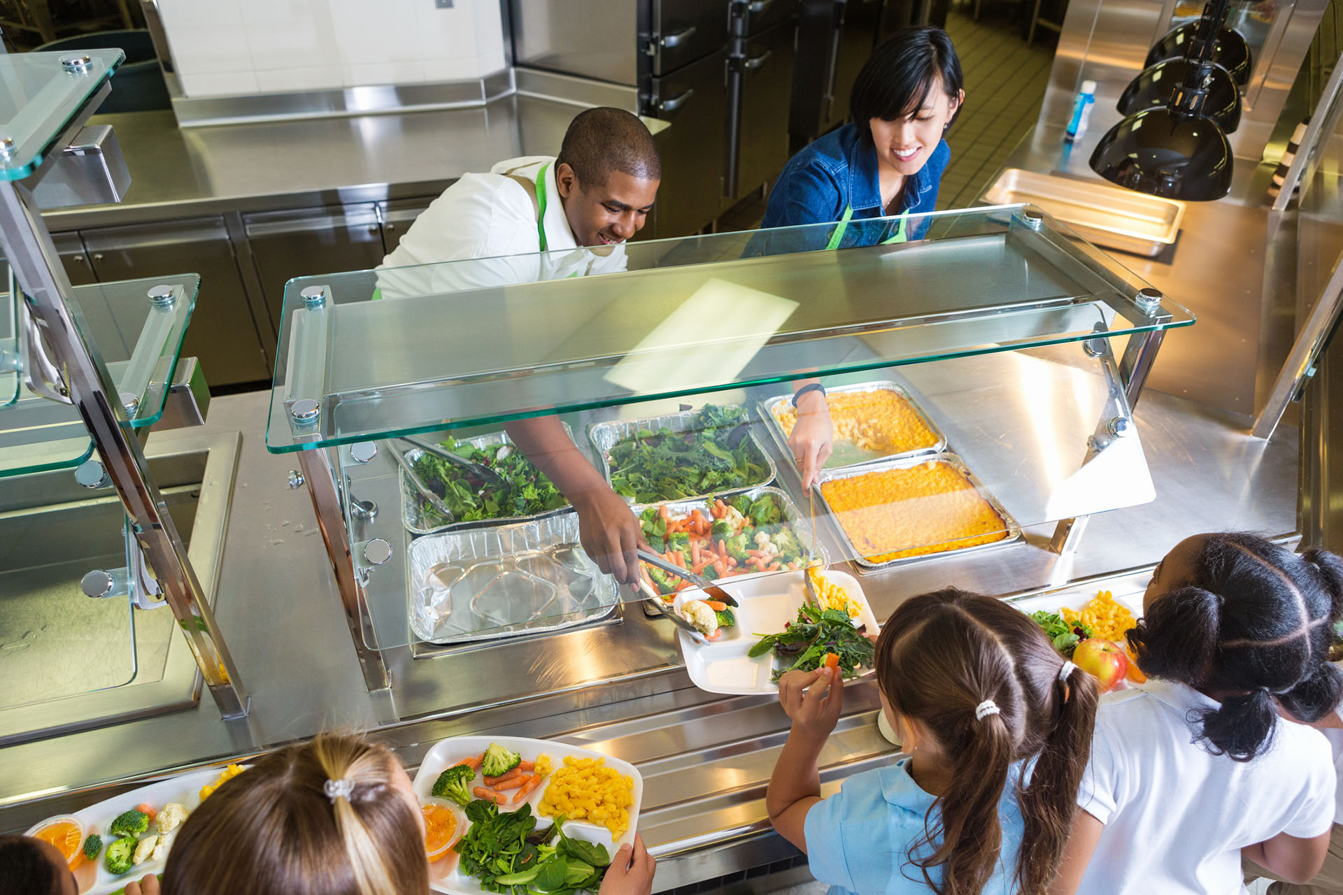 Vue en plongée d'un homme et d'une femme servant des repas à des enfants dans une cantine