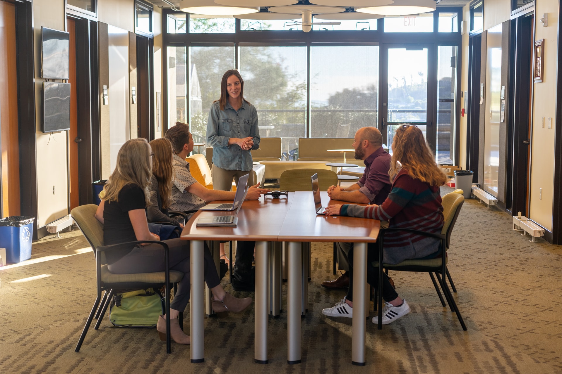 Four people sitting at a table listening to a white woman dressed in blue talking