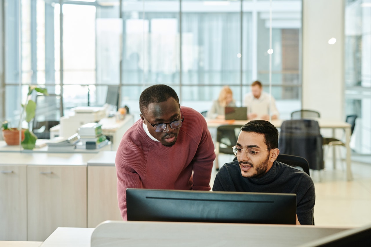 A Black man standing next to an olive-skin man in front of a computer