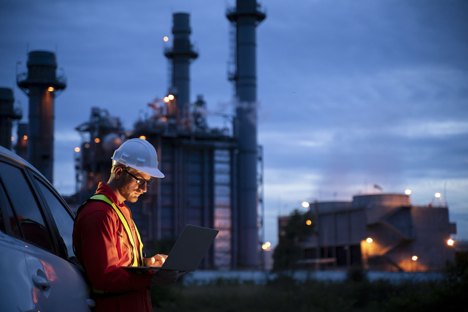 Un homme blanc en gilet orange travaille sur une tablette devant une usine