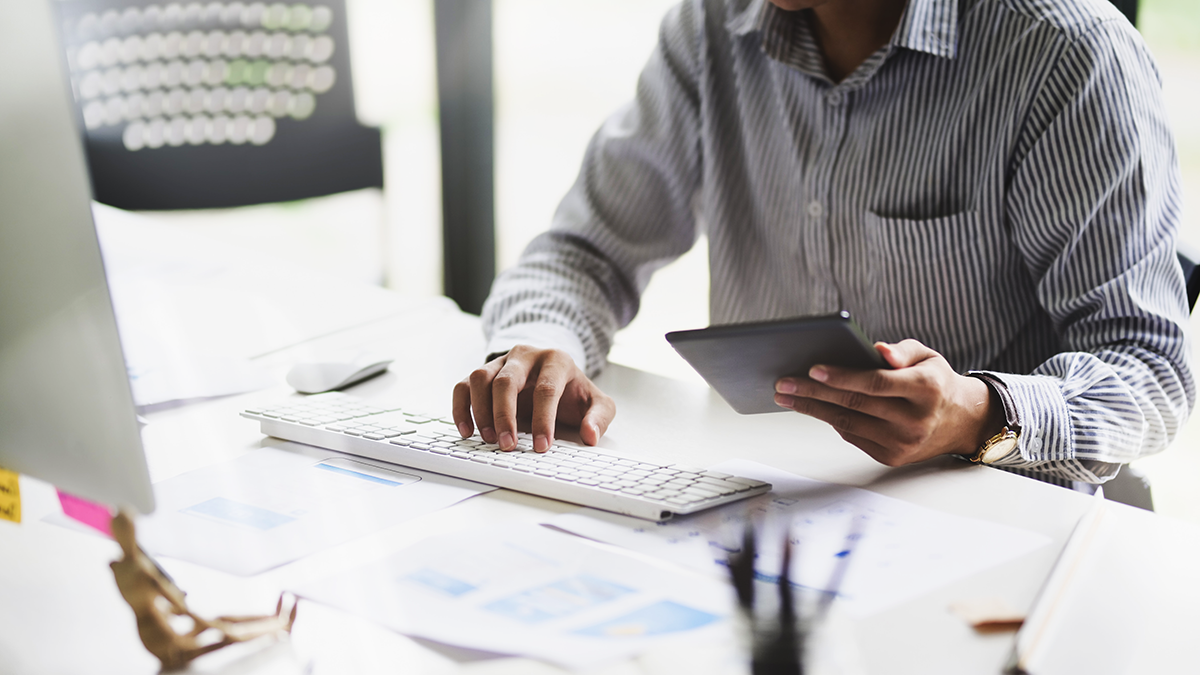 Un'uomo nero al suo tavolo tenendo una tableta e scrivando sul computer