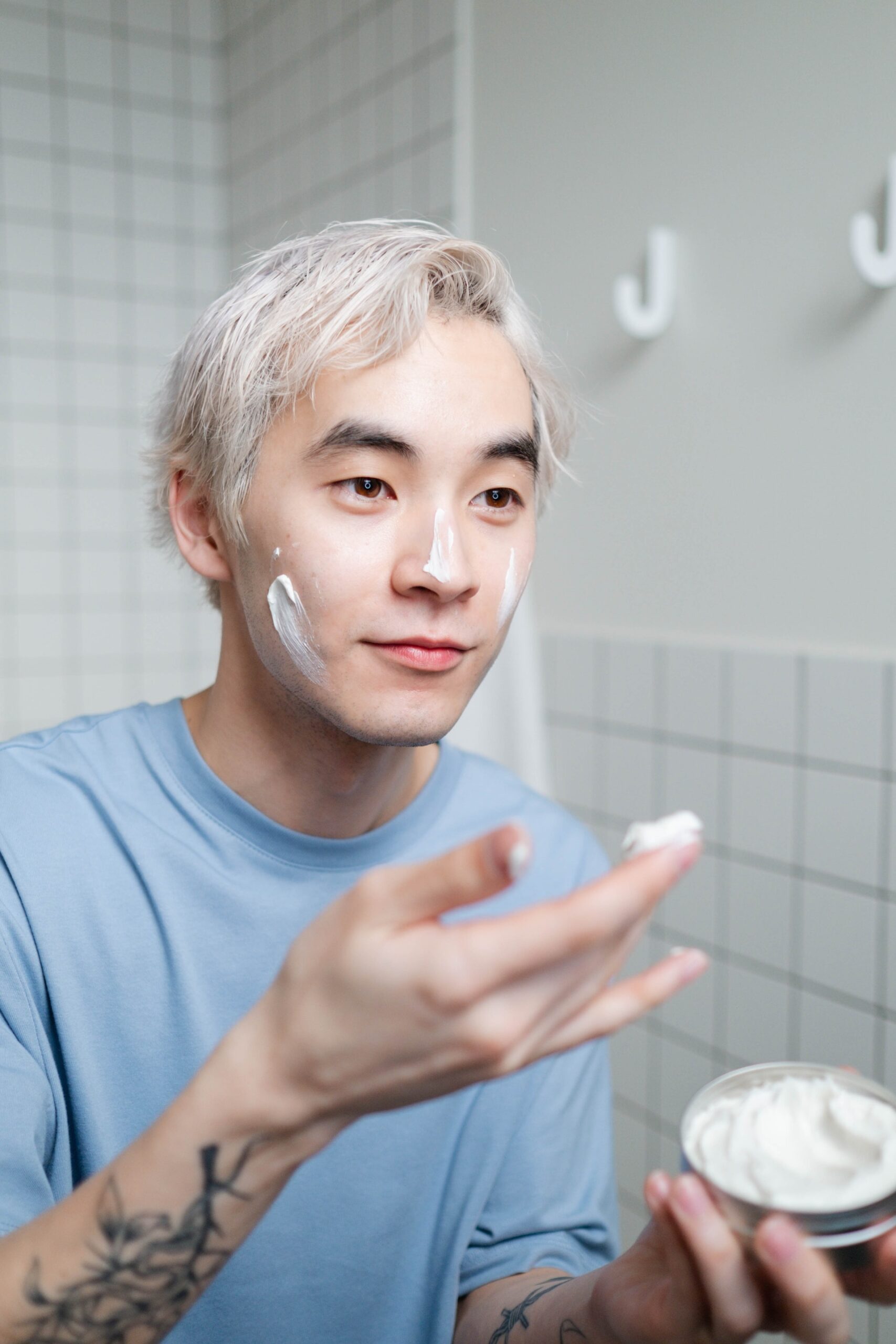 Homme asiatique aux cheveux blonds appliquant de la crème sur son visage