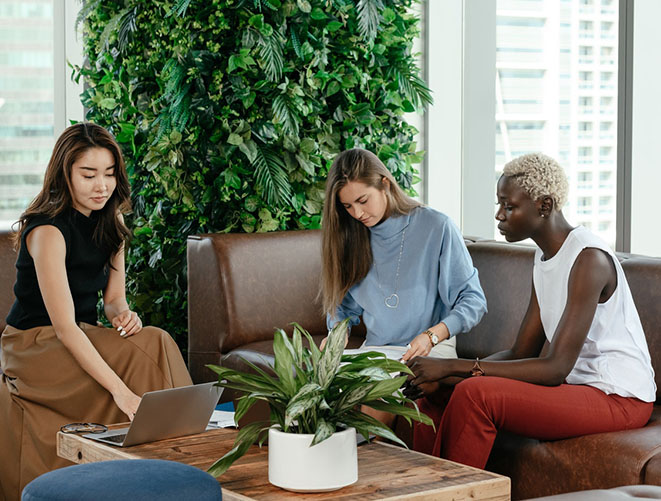 Trois femmes assises autour d'une table basse dans un bureau aux murs végétalisés