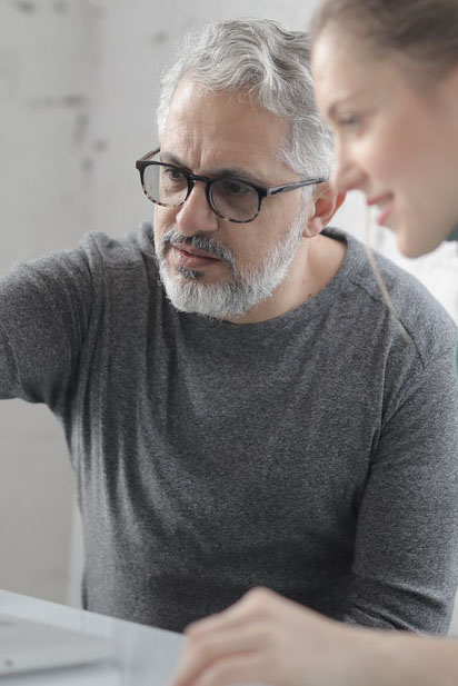 Un homme aux cheveux blancs et une jeune femme regardent un écran d'ordinateur