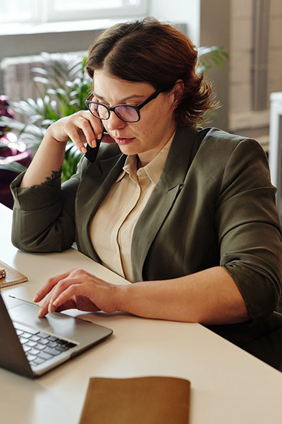 Une femme blanche assise au téléphone regarde son ordinateur portable