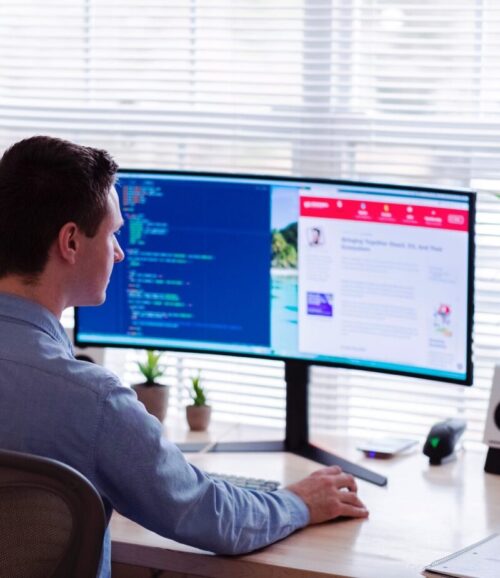 Homme blanc de dos assis devant un écran d'ordinateur, face à une fenêtre