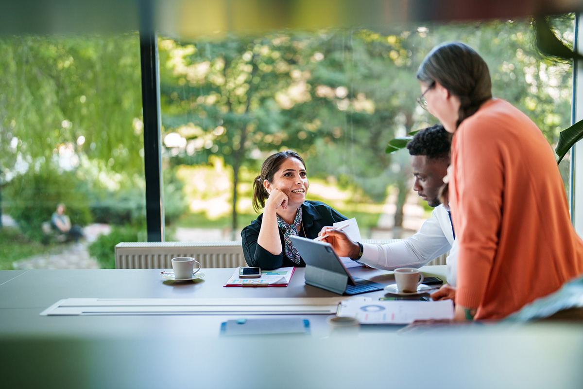 Une femme hispanique de face parle à un homme noir assis à un bureau et à une femme debout de dos
