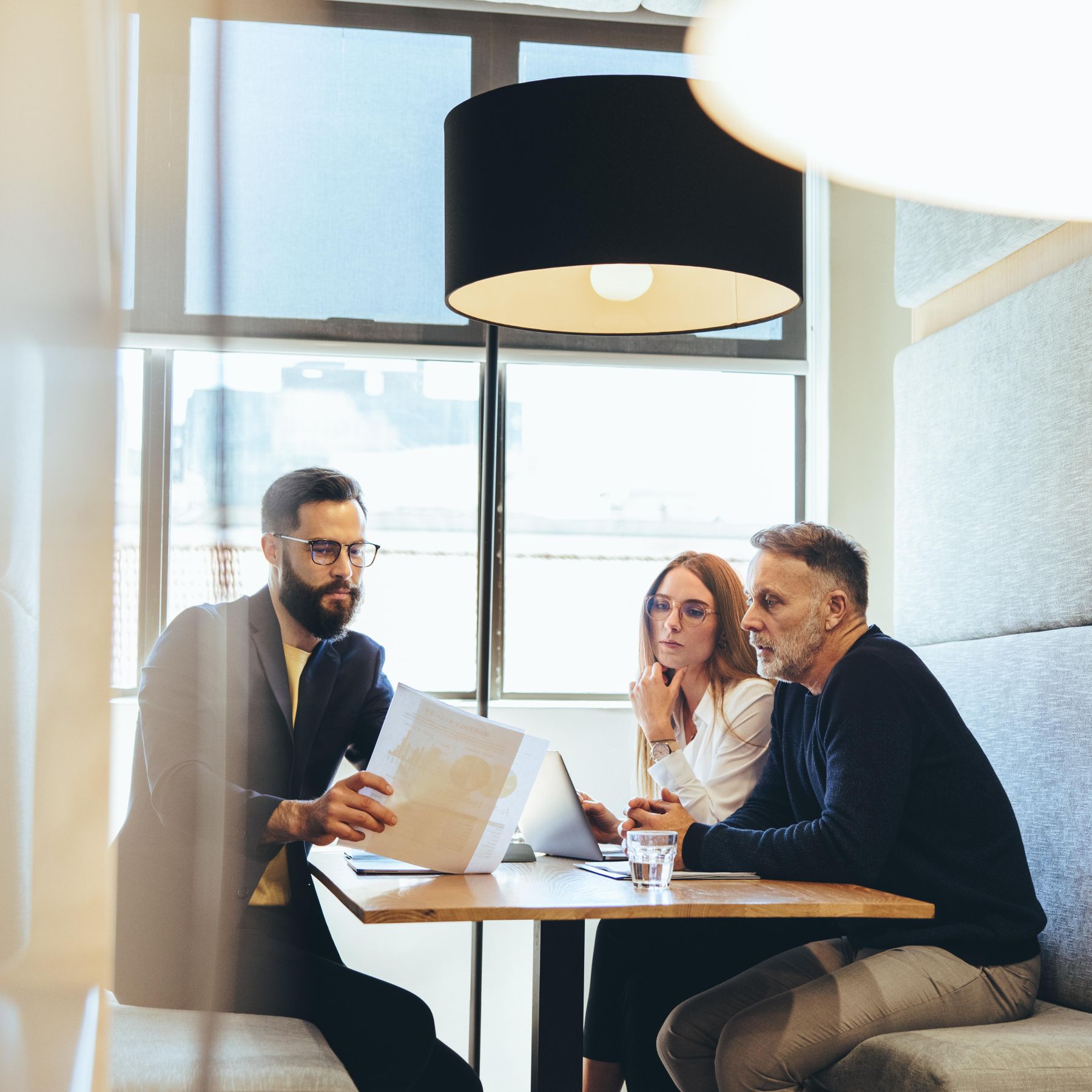 Un homme brun montre un document à une femme rousse et un homme aux cheveux gris