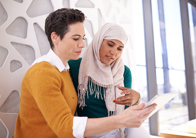 Une femme portant un voile et une femme en pull jaune regardent un document