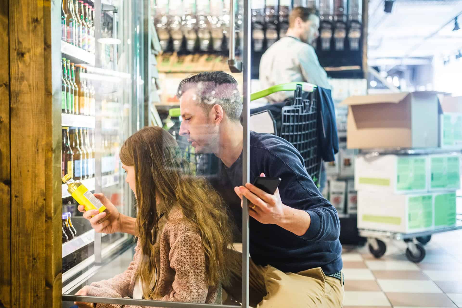 Uomo e bambina davanti a un frigo in un supermercato
