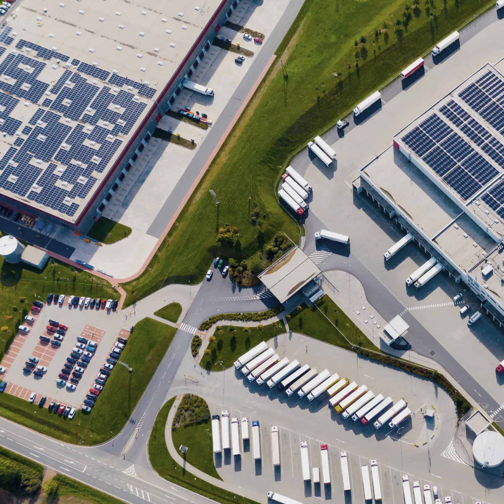 Vue en plongé d'un site logistique avec un parking et deux bâtiments sur lesquels se trouvent des panneaux photovoltaïques