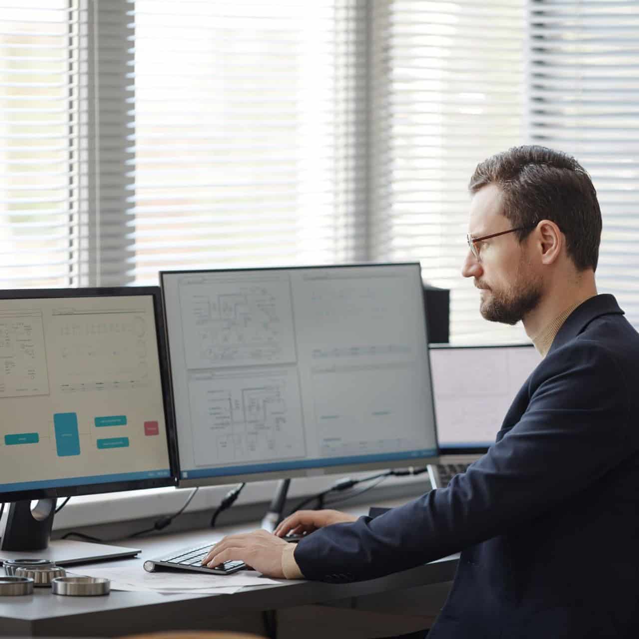 Homme blanc assis à son bureau devant 2 écrans d'ordinateur