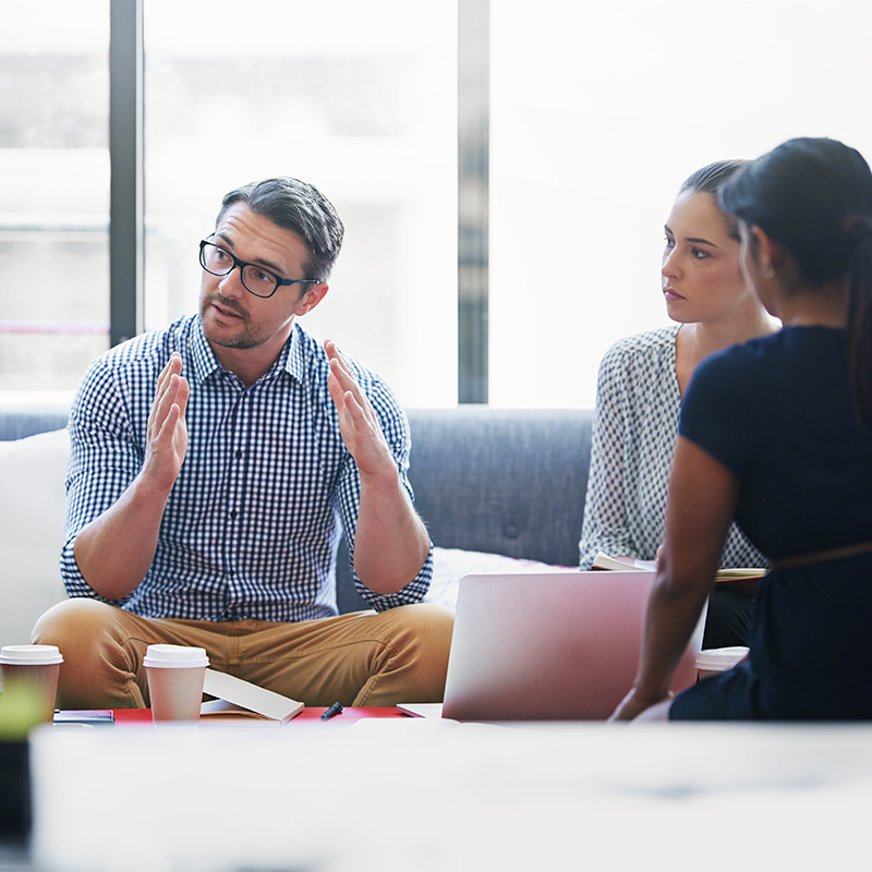 Un homme blanc assis sur un canapé à gauche de deux femmes