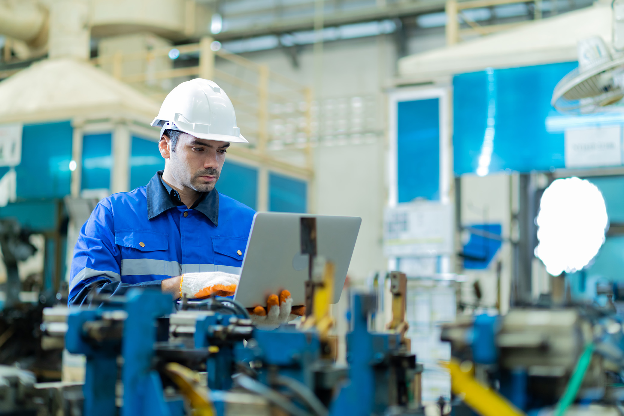 Homme blanc avec un casque de chantier portant un ordinateur portable dans une usine