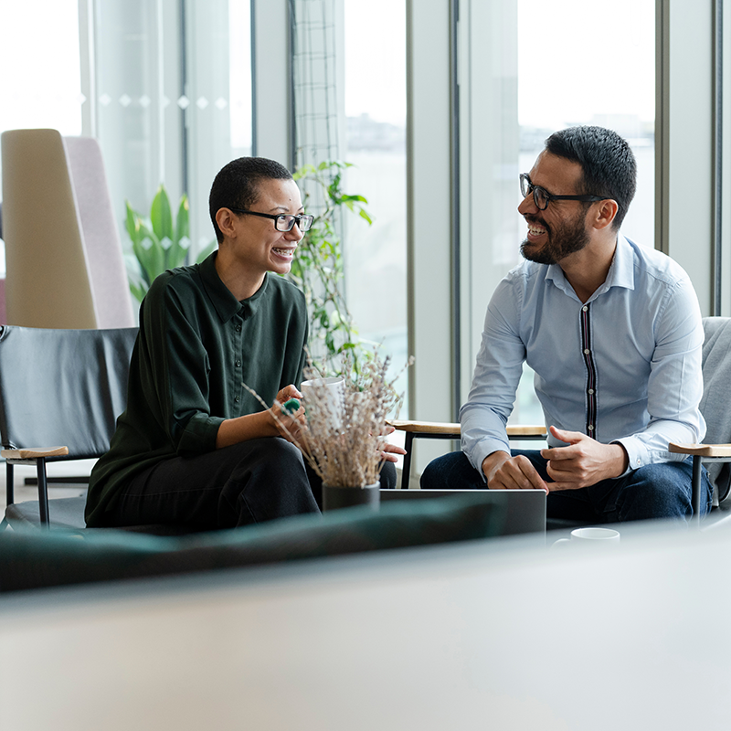 Une femme aux cheveux courts et à la peau mate souriante assise à côté d'un homme blanc et brun souriant également